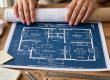 Woman's hands unrolling a blue home blueprint on a wooden desk